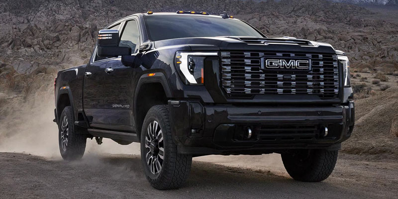 A black 2026 GMC Sierra 3500 being driven on a narrow dusty mountain road.