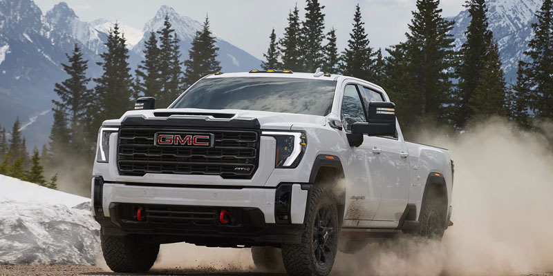 A white 2026 GMC Sierra 3500 HD AT4 truck driving through a snowy mountain landscape.